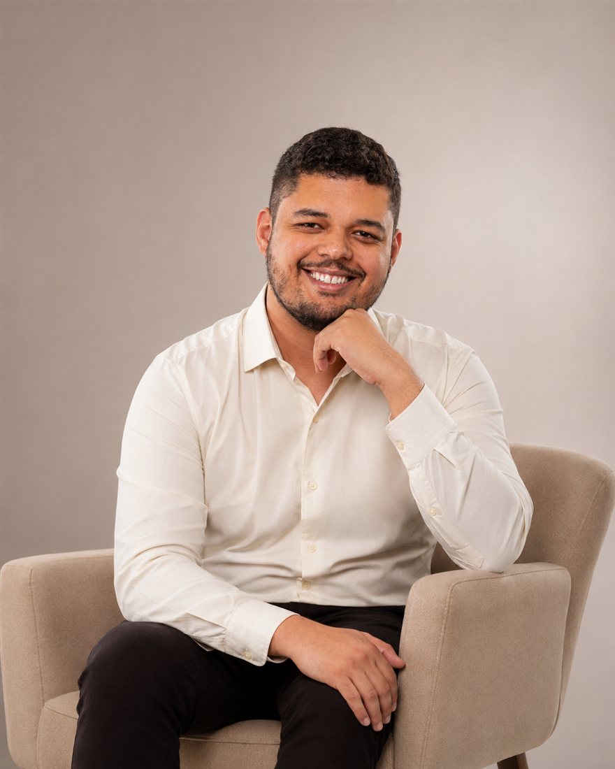 Ramon Alves, psicólogo, sorrindo, sentado em uma poltrona com camisa clara